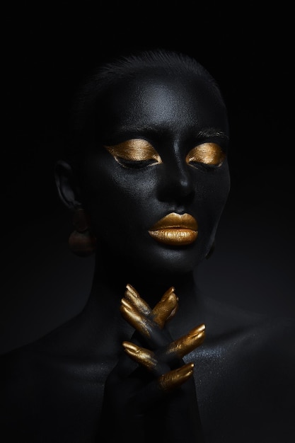 Donna di bellezza dipinta in body art color pelle nera, palpebre labbra trucco oro, unghie della punta delle dita in vernice color oro. Trucco professionale in oro