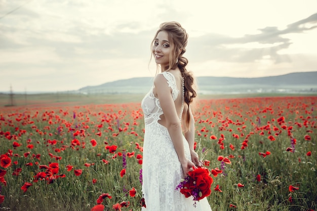 Donna di bellezza nel campo del papavero in vestito bianco. Bella sposa in stile Boho al tramonto in un campo di papaveri rossi