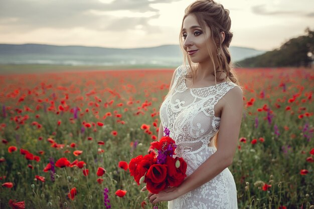 Donna di bellezza nel campo del papavero in vestito bianco. Bella sposa in stile Boho al tramonto in un campo di papaveri rossi