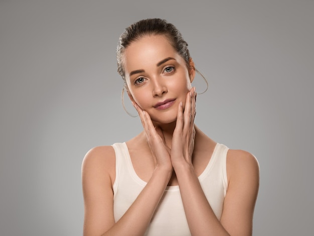 Donna di bellezza pelle sana che tocca il suo viso bella femmina. Colore di sfondo. Grigio