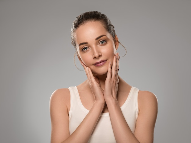 Donna di bellezza pelle sana che tocca il suo viso bella femmina. Colore di sfondo. Grigio