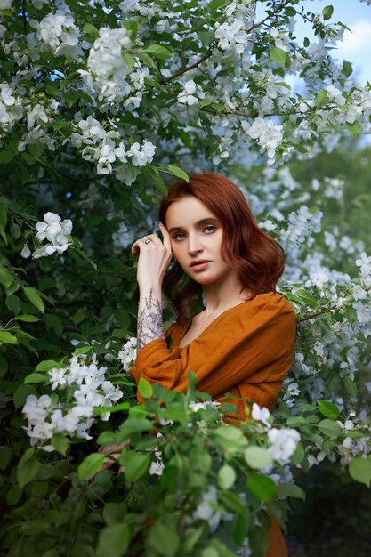 Donna di bellezza ritratto rossa in primavera tra i rami di un albero di mele