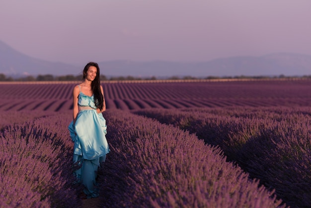 Donna di campo di fiori di lavanda in abito color ciano che si diverte e si rilassa al vento in un campo di fiori viola