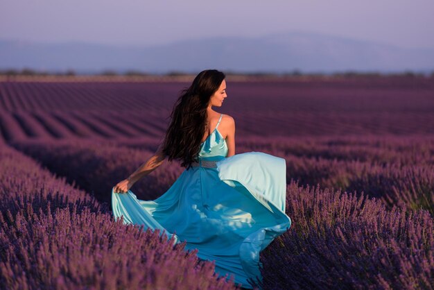 Donna di campo di fiori di lavanda in abito color ciano che si diverte e si rilassa al vento in un campo di fiori viola