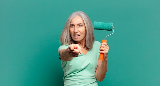 Donna di capelli grigi di mezza età con un rullo di vernice che decora la sua parete