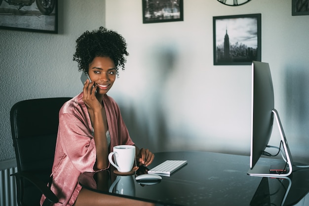 Donna di colore a casa che lavora con il computer e il caffè di mattina