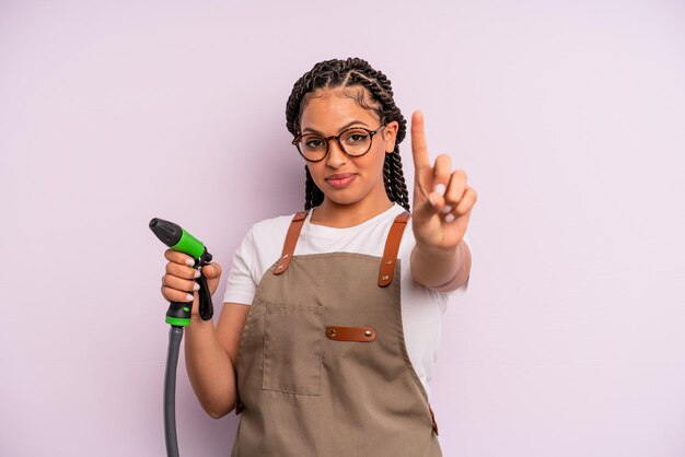 Donna di colore afro che sorride con orgoglio e sicurezza facendo il numero uno. concetto di tubo da giardiniere