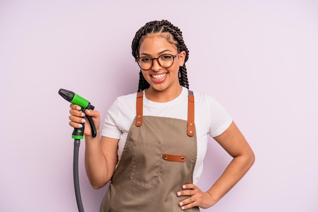 Donna di colore afro sorridente felicemente con una mano sull'anca e sicura di sé. concetto di tubo da giardiniere