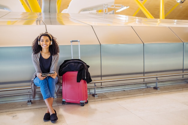 Donna di colore all'aeroporto utilizzando tablet e ascolto musica con le cuffie