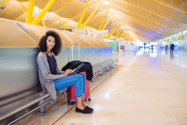 Donna di colore all'aeroporto utilizzando tablet e ascolto musica con le cuffie