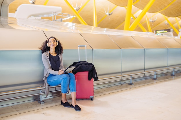 Donna di colore all'aeroporto utilizzando tablet e ascolto musica con le cuffie