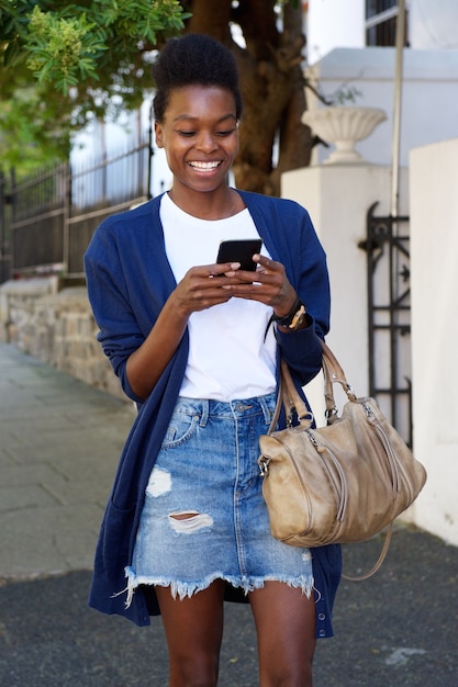 Donna di colore allegra che cammina per strada con il cellulare