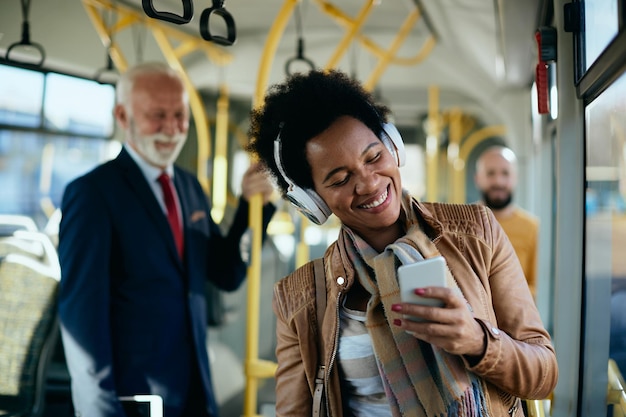 Donna di colore allegra che si diverte mentre utilizza lo smartphone e si sposta in autobus