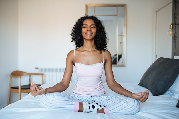 Donna di colore attraente sul letto che meditating