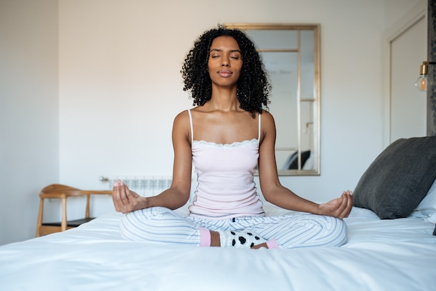 Donna di colore attraente sul letto che meditating