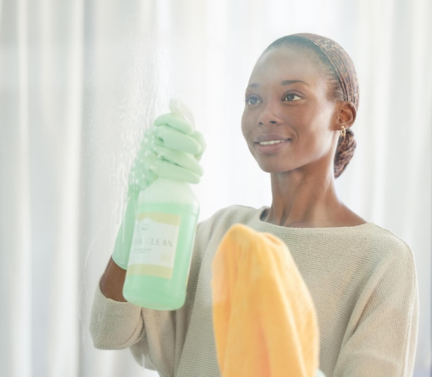 Donna di colore che pulisce e prodotto spray di un detergente che lava uno specchio con un sorriso Cameriera che lavora facendo l'igiene domestica con una bottiglia e un panno per disinfettare il vetro e la finestra dei mobili della casa