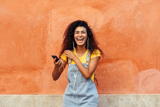 Donna di colore che ride e ascolta la musica con gli auricolari.