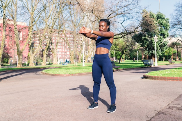 Donna di colore che si scalda e allunga i muscoli per iniziare un allenamento fisico o fare jogging in un parco pubblico