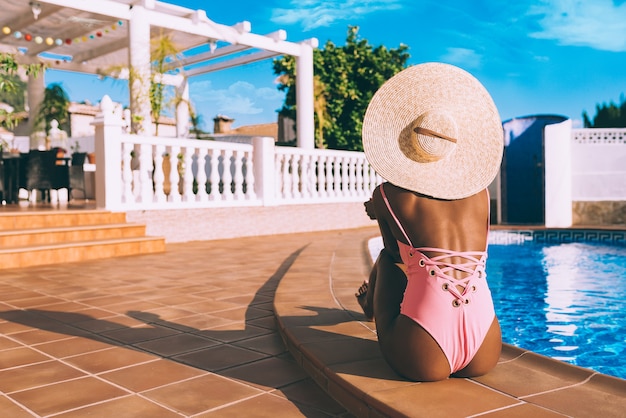 Donna di colore che si siede in un lato della piscina