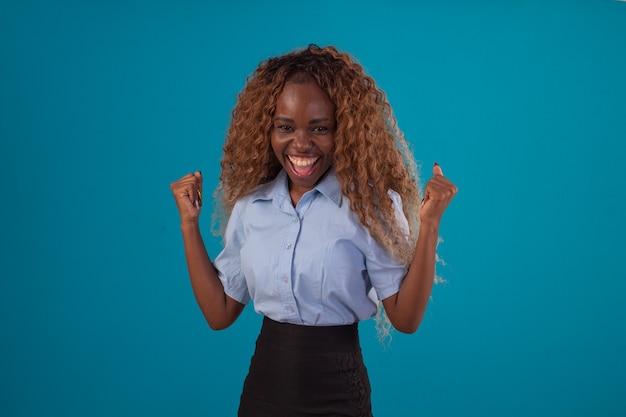 Donna di colore con i capelli ricci in studio fotografico che indossa camicia blu e gonna nera e fa varie espressioni facciali.