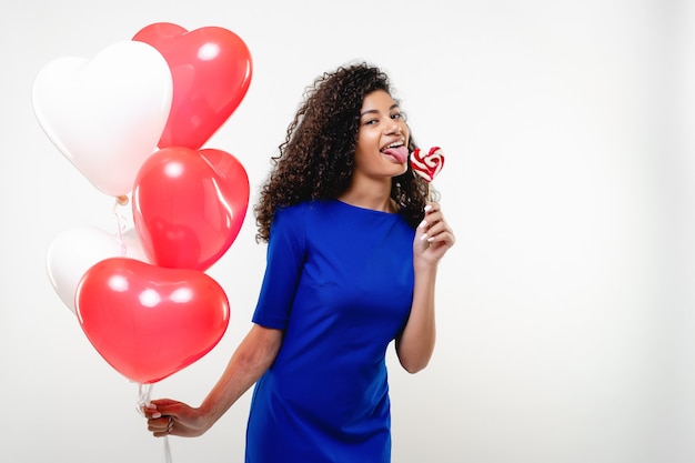 Donna di colore con la caramella del lollypop a forma di cuore e gli aerostati variopinti isolati