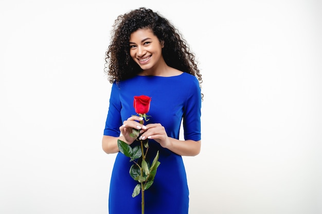 Donna di colore con la rosa rossa che porta vestito blu isolato