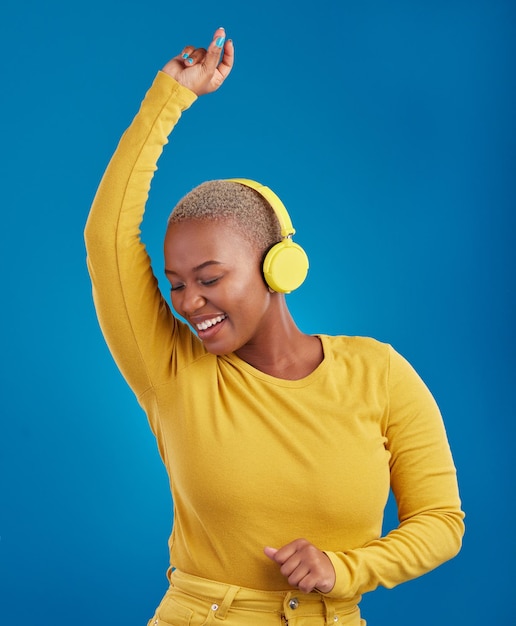 Donna di colore con le cuffie che balla e ascolta musica ritmo e divertimento con libertà su sfondo blu Femmina felice con radio in streaming estetica gialla con danza e spensierata in studio