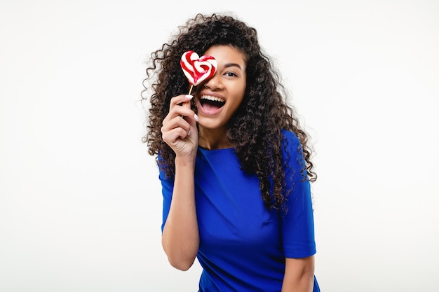 Donna di colore felice con la caramella del lollypop a forma di cuore isolata