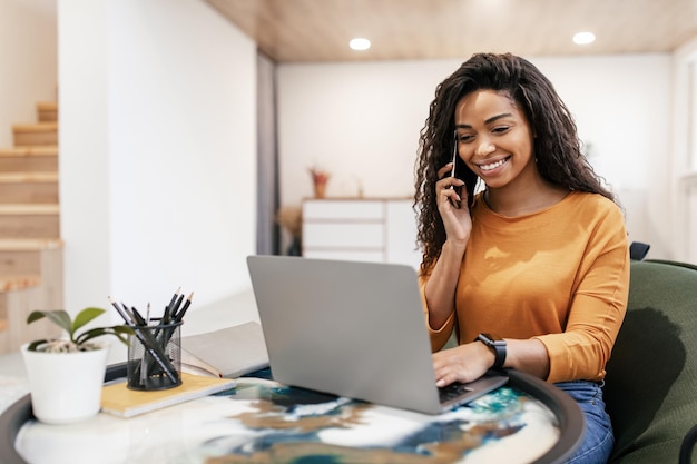 Donna di colore sorridente che lavora e parla al telefono a casa