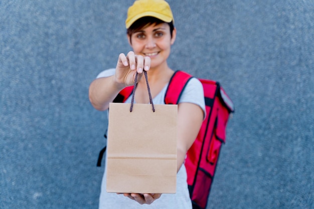 donna di consegna caucasica che consegna la cassetta dei pacchi. Concetto di servizio di corriere. vista orizzontale del pilota felice che consegna a casa un pacco con sfondo grigio.