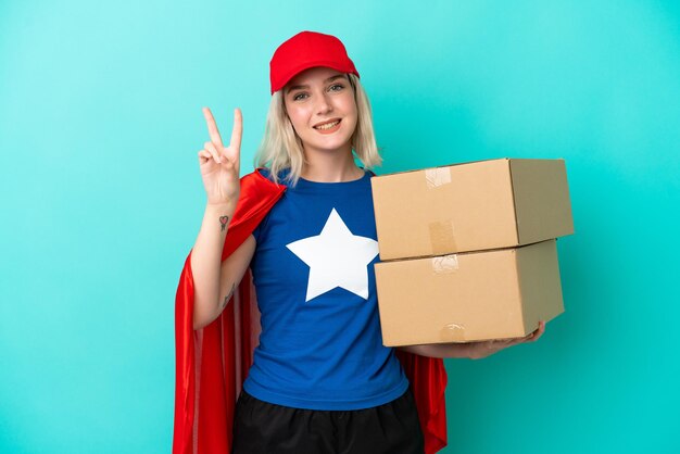 Donna di consegna caucasica Super Hero isolata su sfondo blu sorridente e che mostra il segno di vittoria