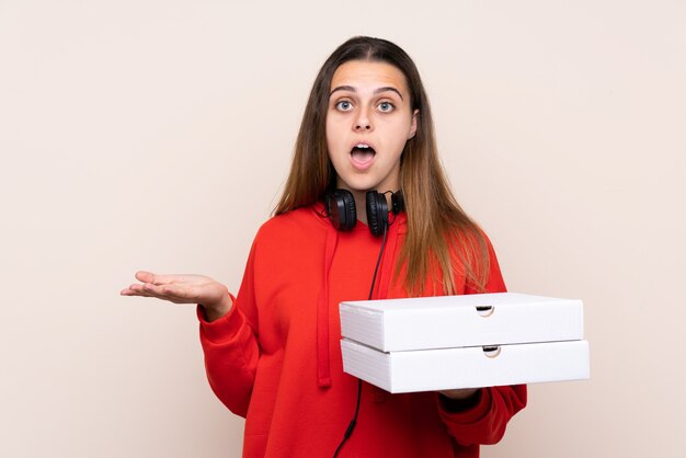 Donna di consegna della pizza che tiene una pizza sopra la parete isolata con espressione facciale colpita