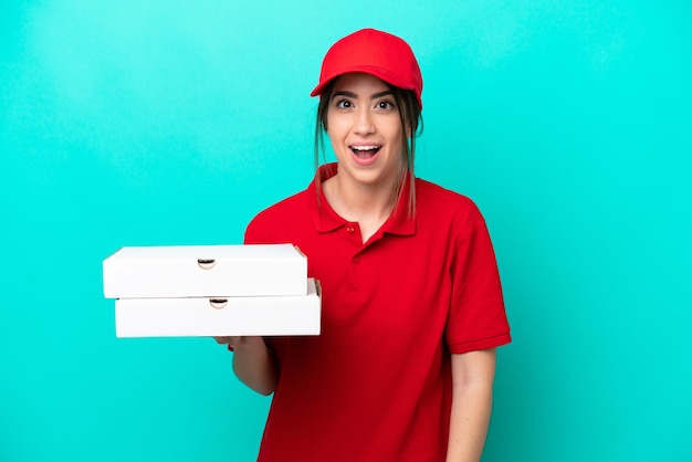 Donna di consegna della pizza con uniforme da lavoro che raccoglie scatole di pizza isolate su sfondo blu con espressione facciale a sorpresa