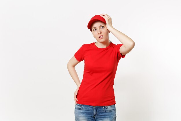 Donna di consegna in uniforme rossa isolata su fondo bianco. Donna scioccata professionale in berretto, t-shirt, jeans che lavora come corriere o rivenditore, mette la mano sul gesto della testa. Copia spazio pubblicitario.