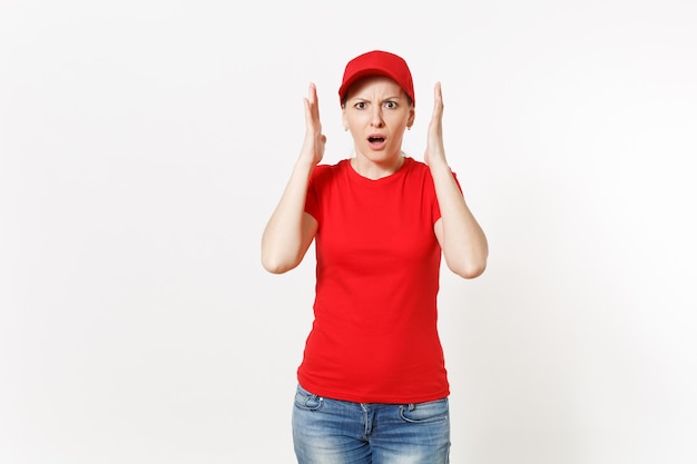 Donna di consegna in uniforme rossa isolata su fondo bianco. Donna scioccata professionale in berretto, t-shirt, jeans che lavora come corriere o rivenditore, tenendosi per mano vicino al gesto del viso. Copia spazio, pubblicità.