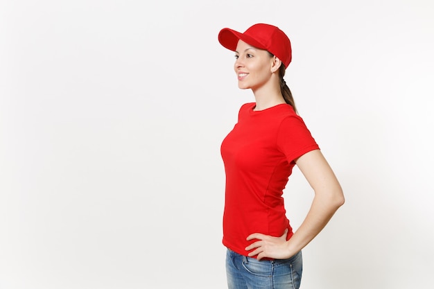 Donna di consegna in uniforme rossa isolata sulla vista laterale del fondo bianco. Femmina professionale in berretto, t-shirt, jeans che lavora come corriere o rivenditore in piedi e guardando da parte. Copia spazio per la pubblicità.