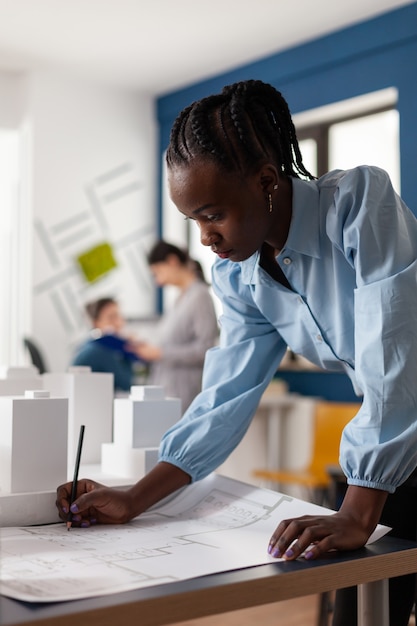 Donna di etnia afroamericana che lavora come architetto in uno studio professionale. Costruttore dell'ingegnere alla scrivania che guarda il piano di cianografia per la costruzione del modello maquette. Progetto di sviluppo