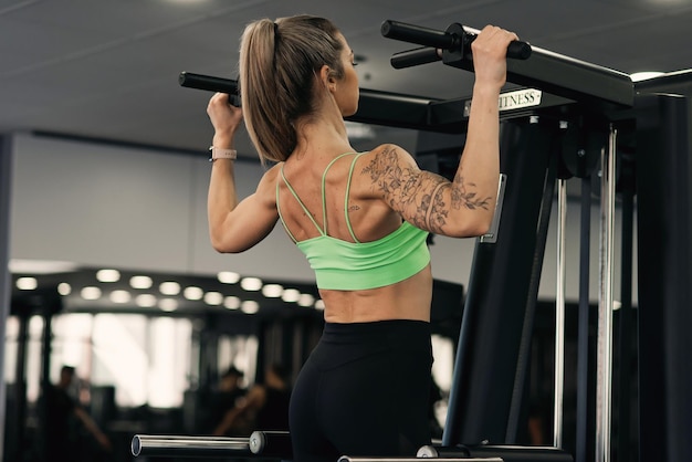 Donna di fitness che fa pullup, esercizio per i muscoli della schiena, allenamento in palestra, allenamento per ragazze atletiche.