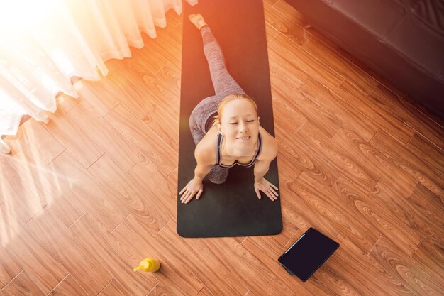 Donna di fitness che si esercita sul pavimento a casa e guarda video di fitness su un tablet