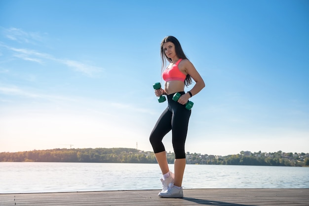 Donna di forma fisica che fa esercitazione mattutina con piccoli pesi del lago