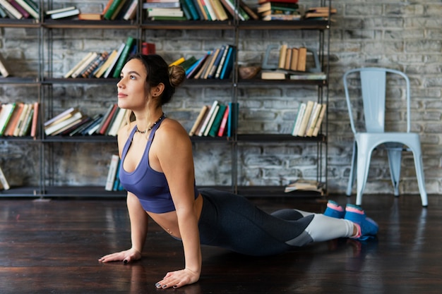 Donna di forma fisica che fa posa della cobra durante l'allenamento di yoga sul pavimento a casa