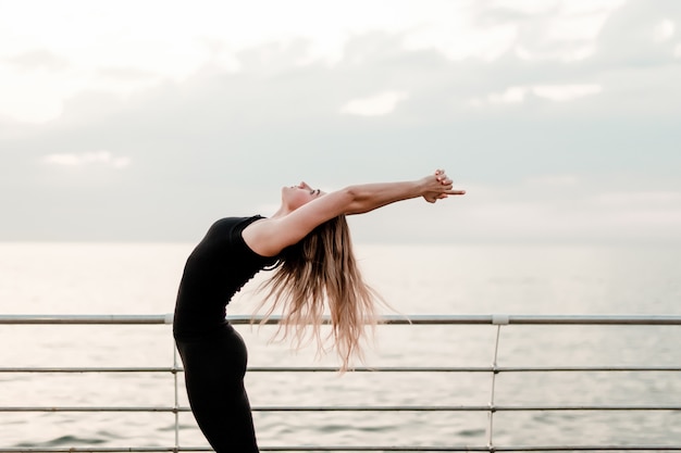Donna di forma fisica che fa yoga e che esercita asana vicino al mare su alba