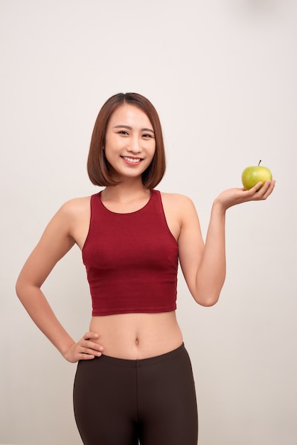 Donna di forma fisica che mangia mela che indossa nastro di misurazione. Donna asiatica / caucasica multiculturale sportiva adatta di forma fisica isolata su bianco. - Immagine