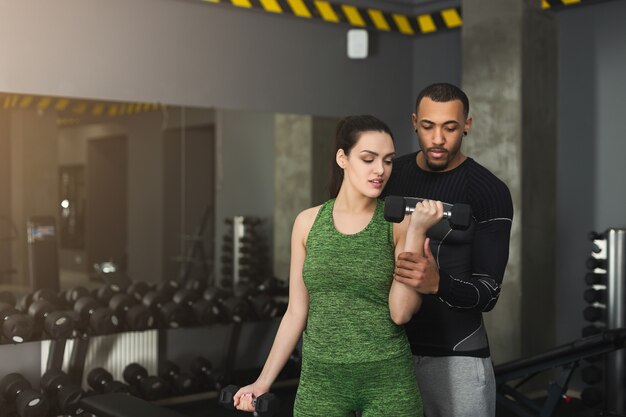 Donna di forma fisica che si allena con il suo personal trainer in palestra. Giovane coppia che fa esercizio di forza per i bicipiti, copia spazio