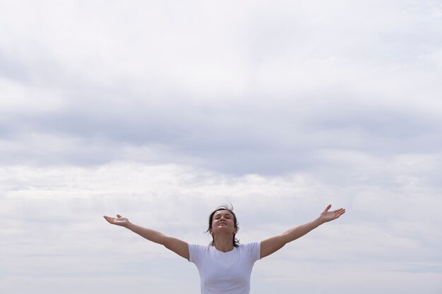 Donna di fronte con camicia bianca alzando le braccia al cielo