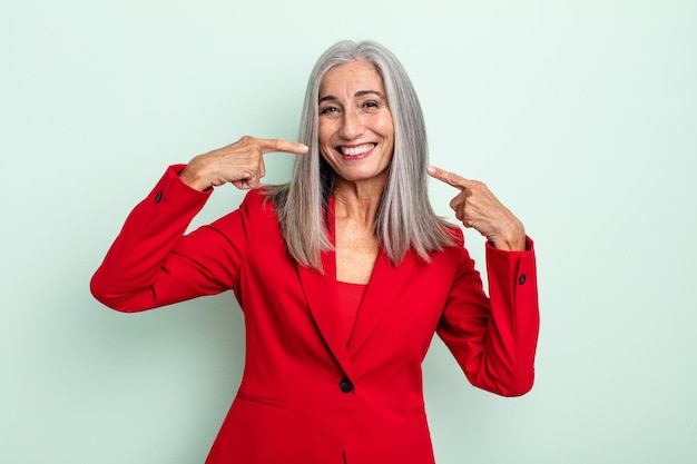 Donna di mezza età capelli grigi sorridente con fiducia che punta al proprio ampio sorriso. concetto di donna d'affari senior