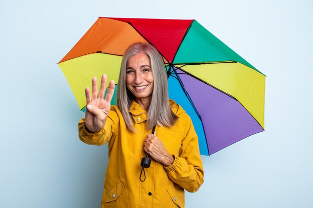 Donna di mezza età capelli grigi sorridente e guardando amichevole, mostrando il numero quattro. concetto di ombrello e pioggia