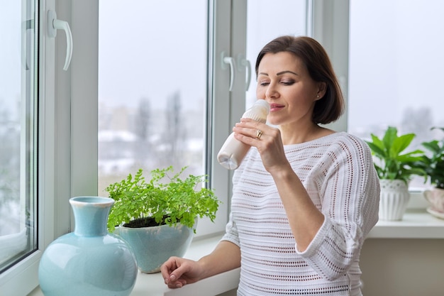 Donna di mezza età che beve latte di yogurt con prodotti lattiero-caseari in bottiglia