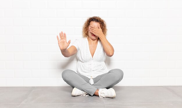 Donna di mezza età che copre il viso con la mano e mette l'altra mano davanti per fermarsi, rifiutando foto o immagini