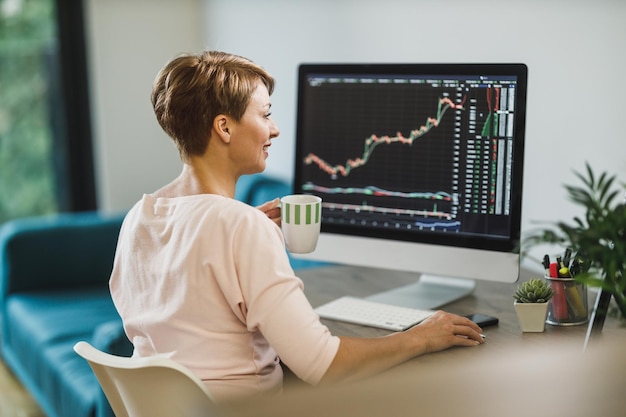 Donna di mezza età che fa trading con criptovaluta mentre lavora al computer a casa. Controlla i suoi investimenti nei mercati azionari.